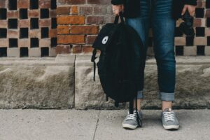 person standing near brown concrete wall with black backpack in hand