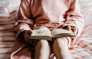 child reading book sitting on red and white striped bedspread