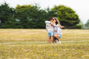 a mother with her arm around her child, standing in the grass