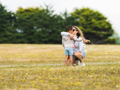 a mother with her arm around her child, standing in the grass