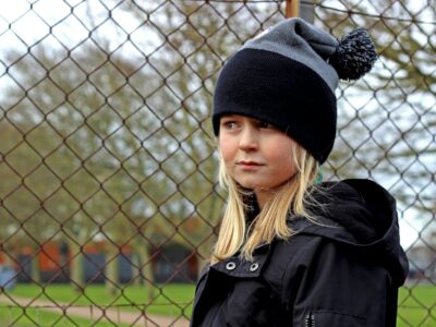 girl in black and grey knit hat and black coat standing near gray metal fence during daytime