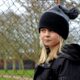 girl in black and grey knit hat and black coat standing near gray metal fence during daytime