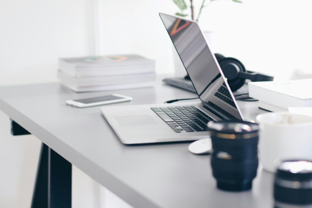 silver MacBook Pro on white desk with coffee cup and phone