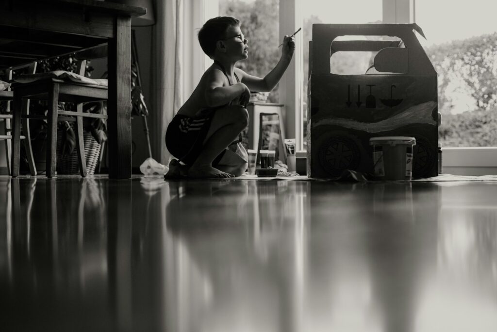 young boy sitting on floor at home painting something