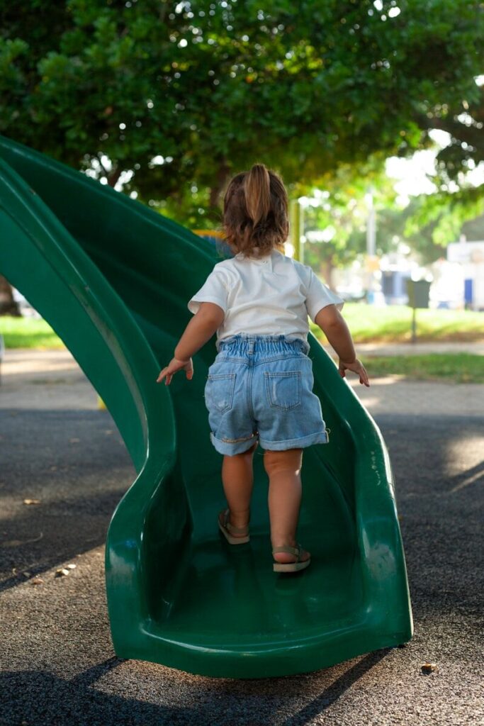 a little girl playing on a green slide